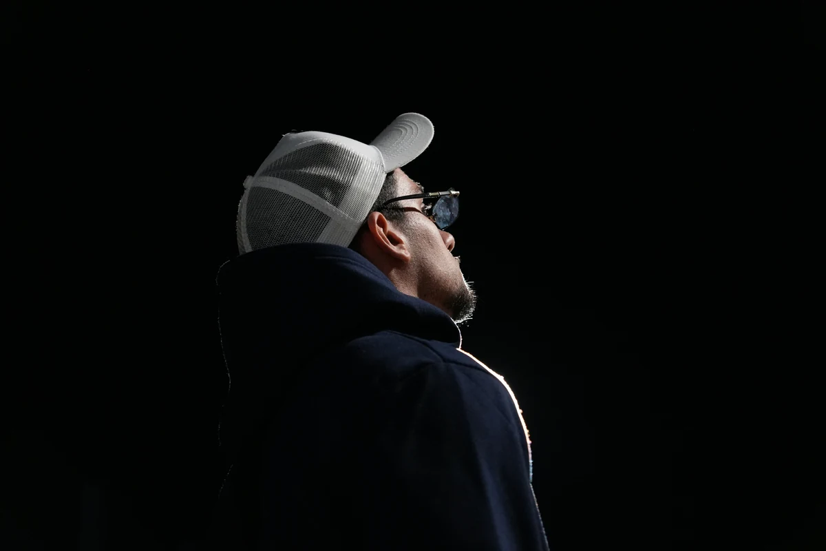 Retrato de espaldas y de perfil sobre fondo negro, con un filo de luz recortando la sudadera y la gorra